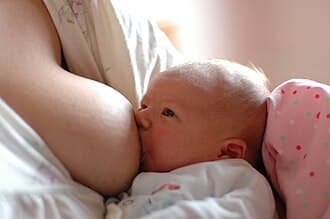 bébé allaité, tête contre le sein de sa mère, main sur le dos