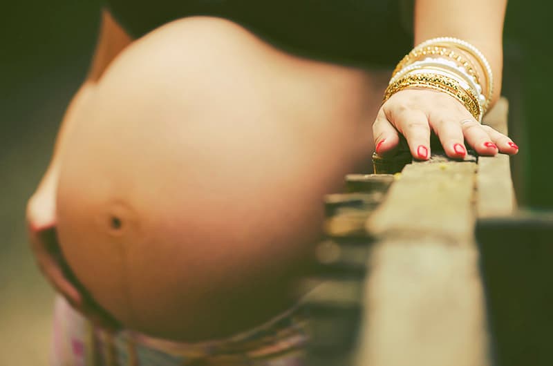 femme enceinte contre une rambarde, mains sur le ventre